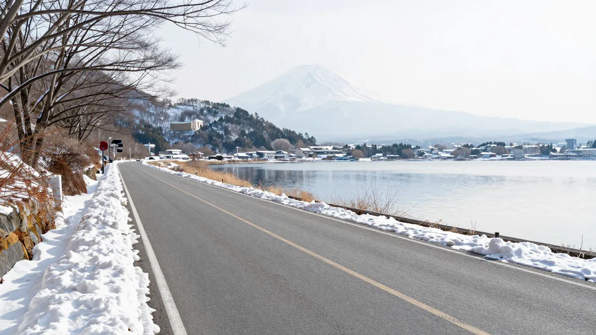雪が残る湖畔の道路と、遠くに雪をかぶった富士山が見える冬の風景